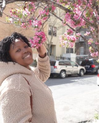 A woman smiles next to a tree with bright pink flowers.