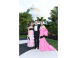 Three people in pink gowns and black suits pose for a photo outdoors