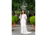 A person with long dark hair poses for a photo in a flowing white dress