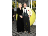 Two people in evening wear pose for a photo in front of a large yellow sphere