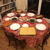 A table setting of foods in a room full of books, sitting on a decorated red tablecloth