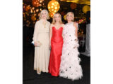 Three people in red and white gowns pose for a photo at an evening event