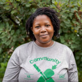 Headshot of Liana Castillo Vicente wearing a grey shirt with green writing that says "Community Ya Dig" with green graphics of a carrot.