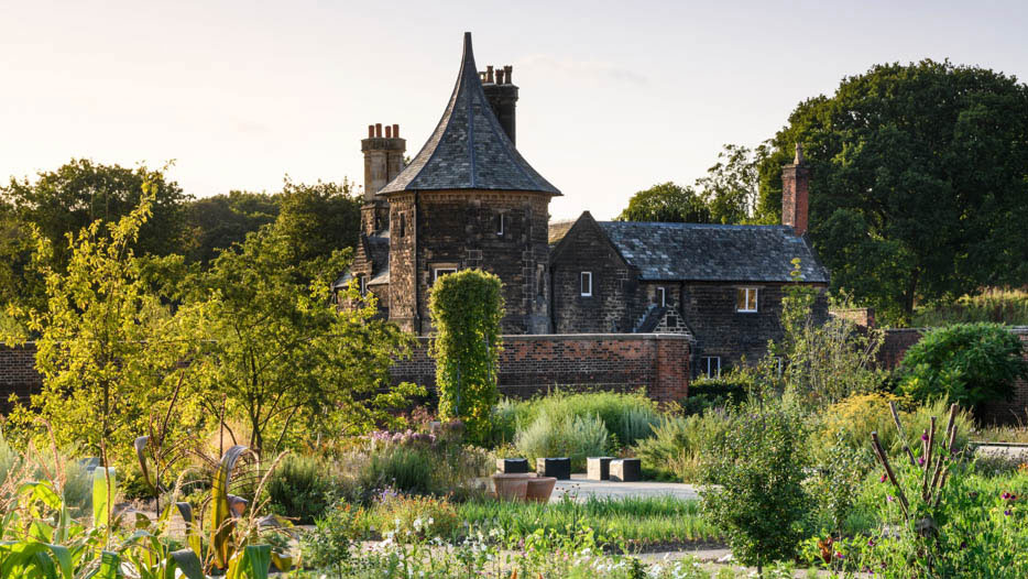 A classical manor sits among sprawling green gardens on a sunny day
