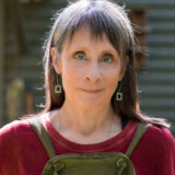 a close up of a person with a burgundy shirt and drop down earrings with grey hair