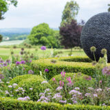 A bright green garden with purple and pink flowers and a decorative sphere made of smooth rocks.