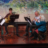 three members of the Bronx Arts Ensemble playing musical instruments on stage in Ross Hall at NYBG