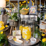 springtime display at NYBG Shop featuring yellow flowers, yellow vase decorated with white flowers, various little decorative trays, and books