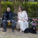 A still of Sigourney Weaver in a white skirt and floral cardigan sitting on a bench alongside Joel Edgerton, dressed in all black.