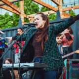 a person in a teal leopard jacket singing on a stage with a band