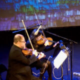 A pair of violinists perform on a darkened stage