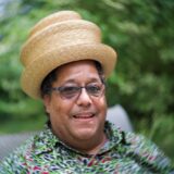 A person in a straw hat poses for a photo outdoors