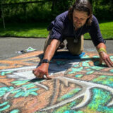 Chalk artist Ben Young creating a chalk art piece on the ground outside featuring green leaves