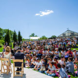 a large group of adults and children gathered at the Edible Academy Amphitheater listening to people talking on a stage