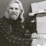A black and white photo of a person with long hair and a beard posing for the image