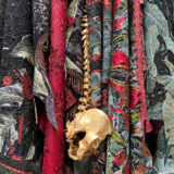 a close up shot of red, green, black, and grey patterned tapestry featuring a small skull and spine hanging in the middle