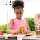 a young person in a pink top creating art with yellow and red stampers