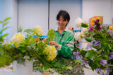 a person in a long sleeved green shirt smiles at a bouquet of fluffy yellow flowers in a classroom