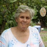 A person in a white and blue shirt, with short gray hair, poses for a photo outdoors