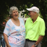Two people in summer clothes pose for a photo, laughing with their arms around each other