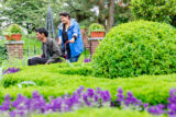 a person in a blue raincoat pushes another person in a wheelchair who is wearing a grey button down and black jeans
