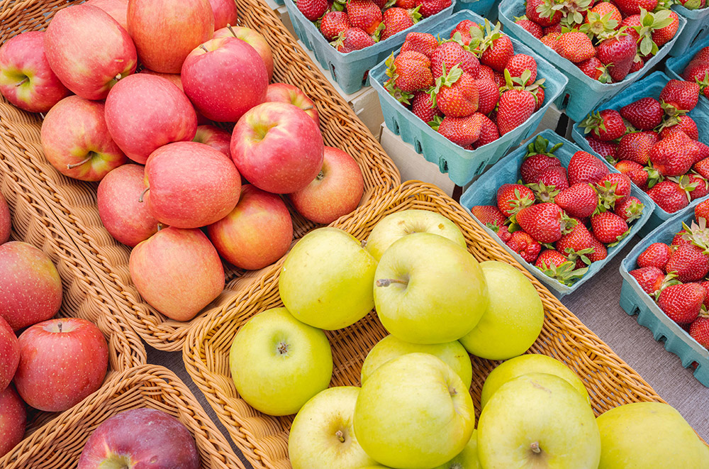 A selection of yellow and red apples boxed up next to cartons of bright red picked strawberries