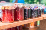 several jars of jam are placed in a row on a wooden shelf