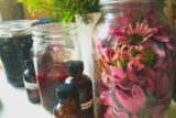 there are several jars and bottle on a table, with one jar filled with pink flowers