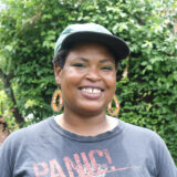 A person in a black shirt and baseball cap poses for a photo outdoors