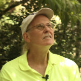 A person in a baseball cap and bright yellow shirt poses for a photo outdoors