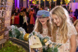 Two children with blonde hair watch as a model train passes through a miniature scene