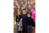 A family of four wearing black winter clothes pose for a photo in a holiday setting