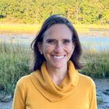 A person in a yellow turtleneck sweater poses outdoors for a photo