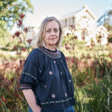 A person in a blue frock poses for a photo in a sunny classical garden