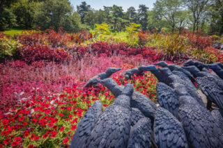 A garden with bright red flowers and leaves with a group of sculpted vultures standing over it.