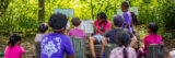 a person in a pink shirt sitting down reading a book to a group of young children