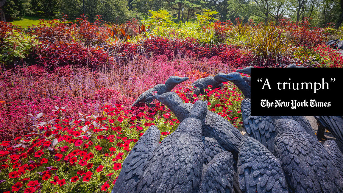 A flock of sculpted black vultures sits in a field of red flowers and foliage