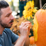 a person paints a carved jack-o-lantern with a human face