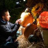 a person in a jacket carving into a pumpkin under a light