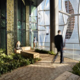 People sit in a relaxing space within a skyscraper, surrounded by seating and green plants