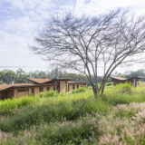 Low orange and brown buildings with V-shaped rooftops sit among lush green foliage