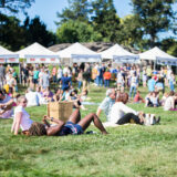 people lounging in a field with beer vendors set up in white tents in the background