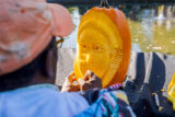 a person in an orange hat carving a face into a tall oval pumpkin