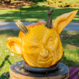 a carved pumpkin with an angry human face and large pointy ears