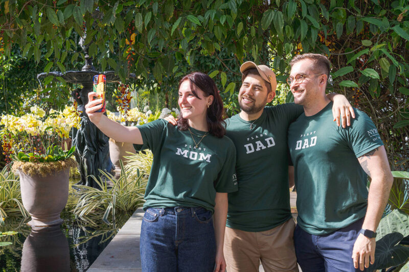 Three people taking a selfie wearing green shirts with white lettering.