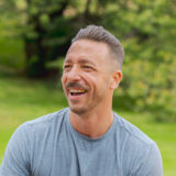 A person with short dark hair and a mustache poses for a photo outdoors