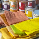 A selection of colorful orange and yellow folded cloth surrounded by powdered dyes in jars
