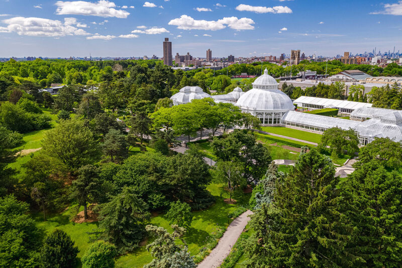 An aerial view of a lush green garden with a white conservatory, and a city skyline visible in the distance