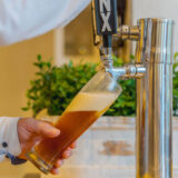 a person in a white shirt pouring beer from a tap into a tall glass