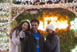 three young people take a selfie in front of a NYBG GLOW neon sign